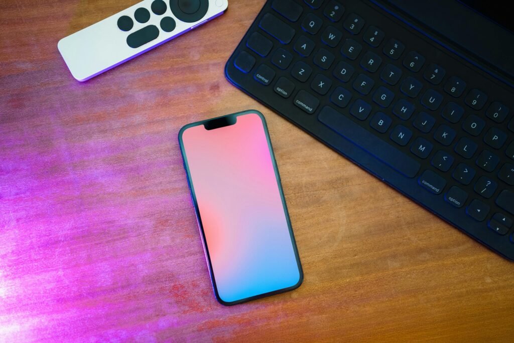 A sleek workspace setup featuring a smartphone, keyboard, and remote on a wooden desk.